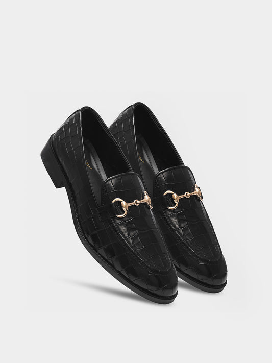 Black loafers with gold horsebit detail on a light gray background