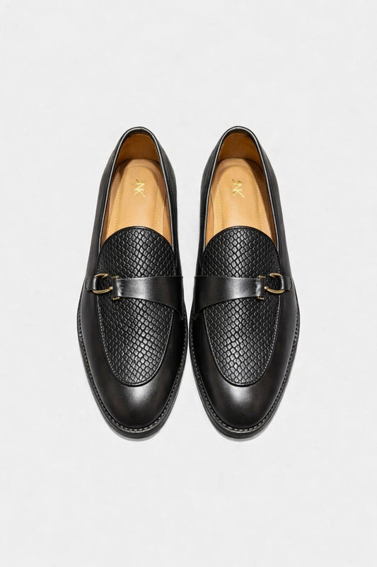 Pair of black loafers with gold buckles on a light gray background