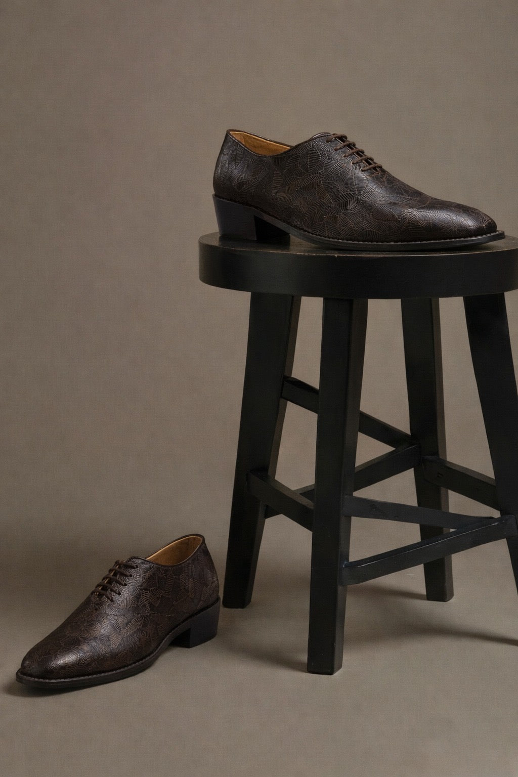 Pair of brown leather shoes on a black stool against a beige background