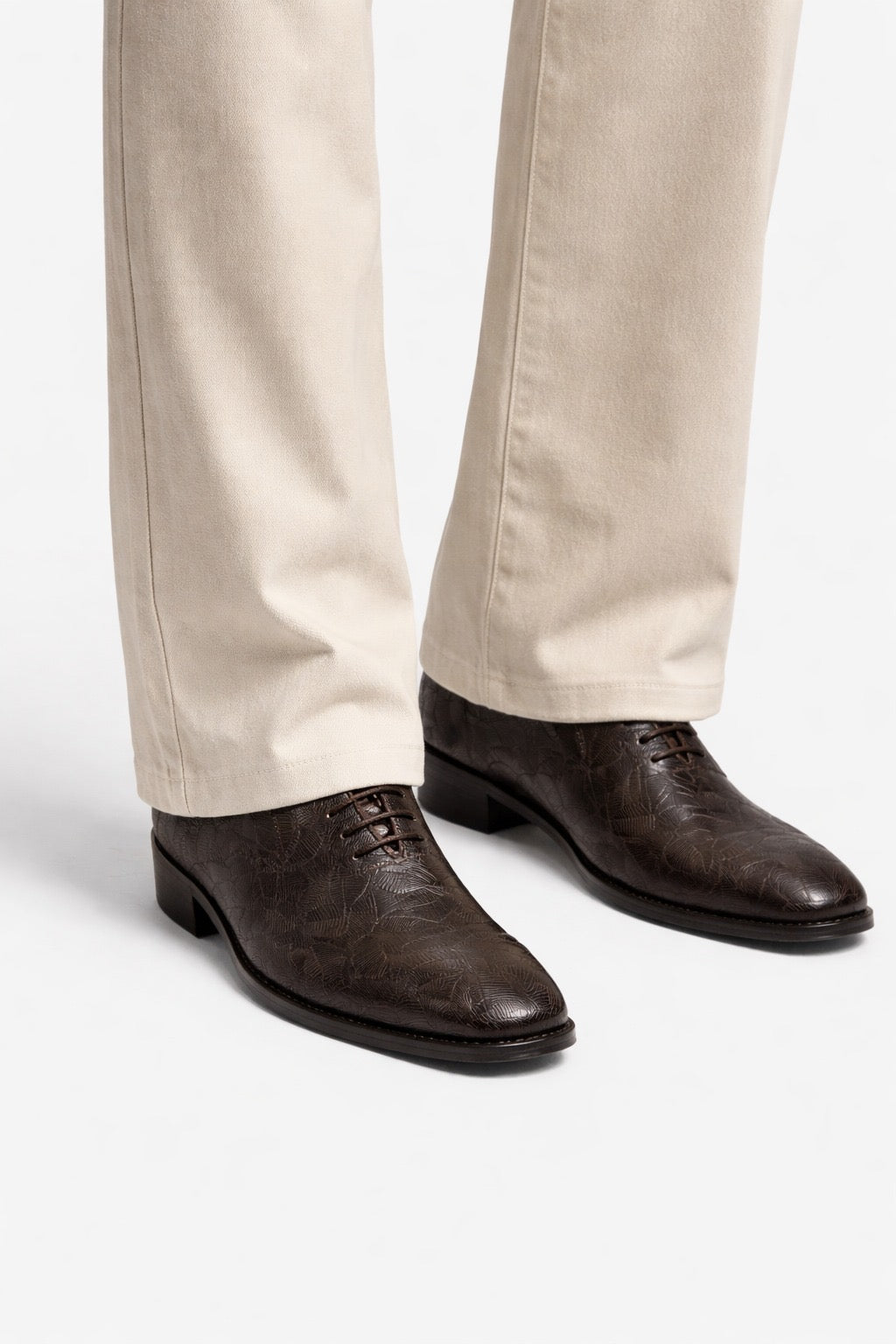 Brown dress shoes worn with beige pants on a white background