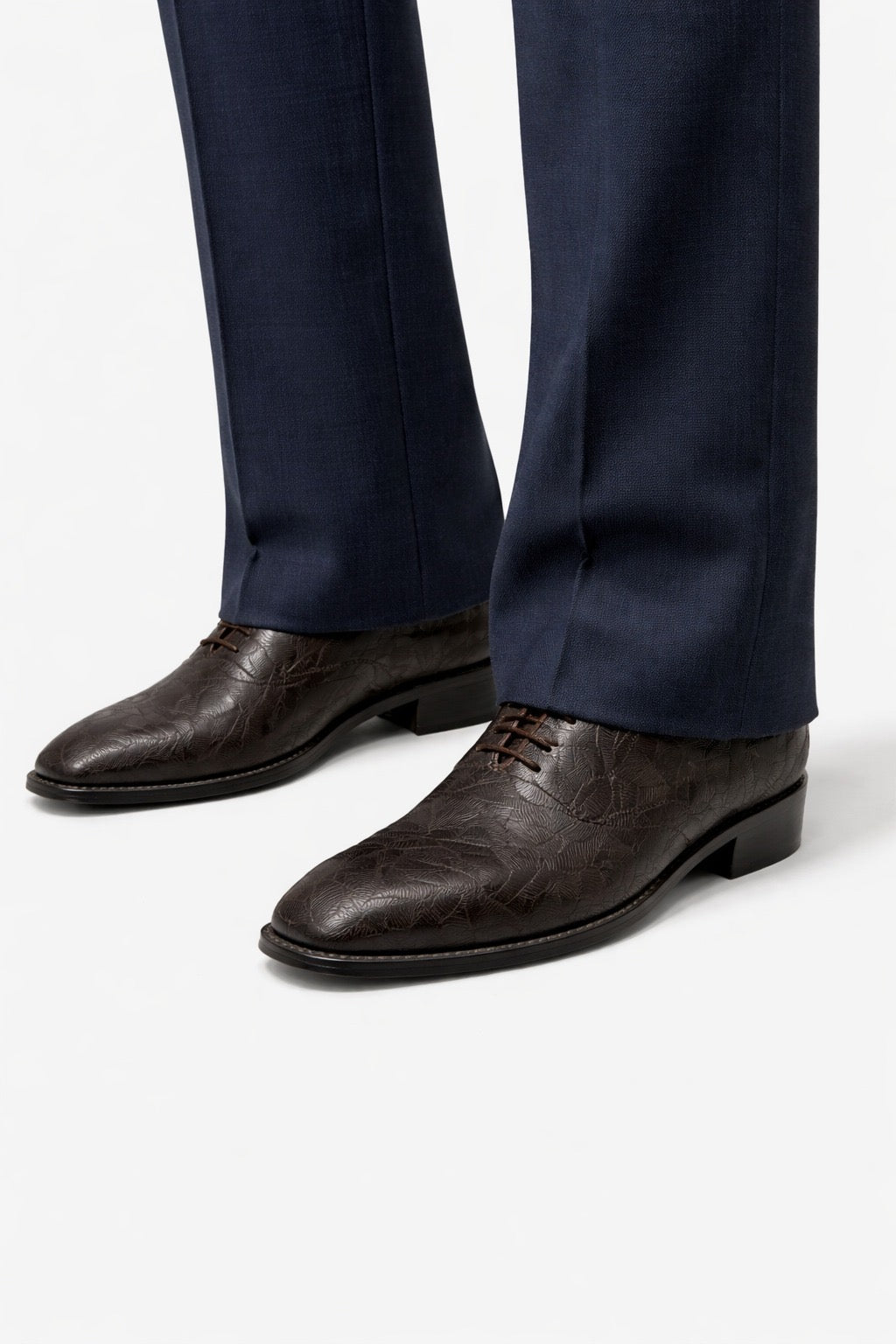 Brown dress shoes worn with navy pants on a white background