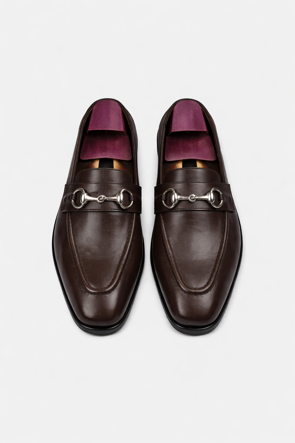 Pair of brown leather loafers with silver horsebit details on a light gray background