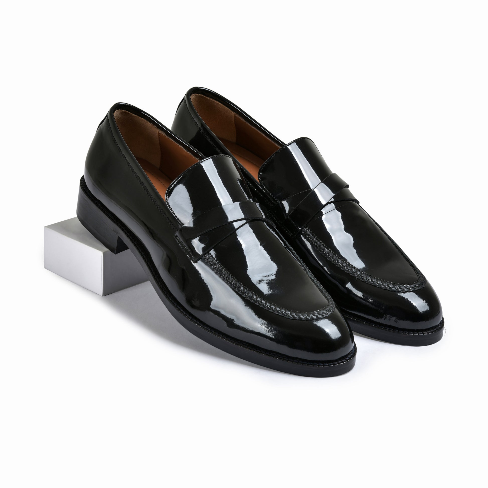 Pair of black patent leather loafers on a white background