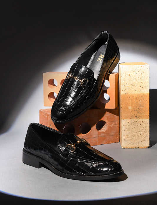 Black glossy loafers on a gray surface with a wooden block in the background