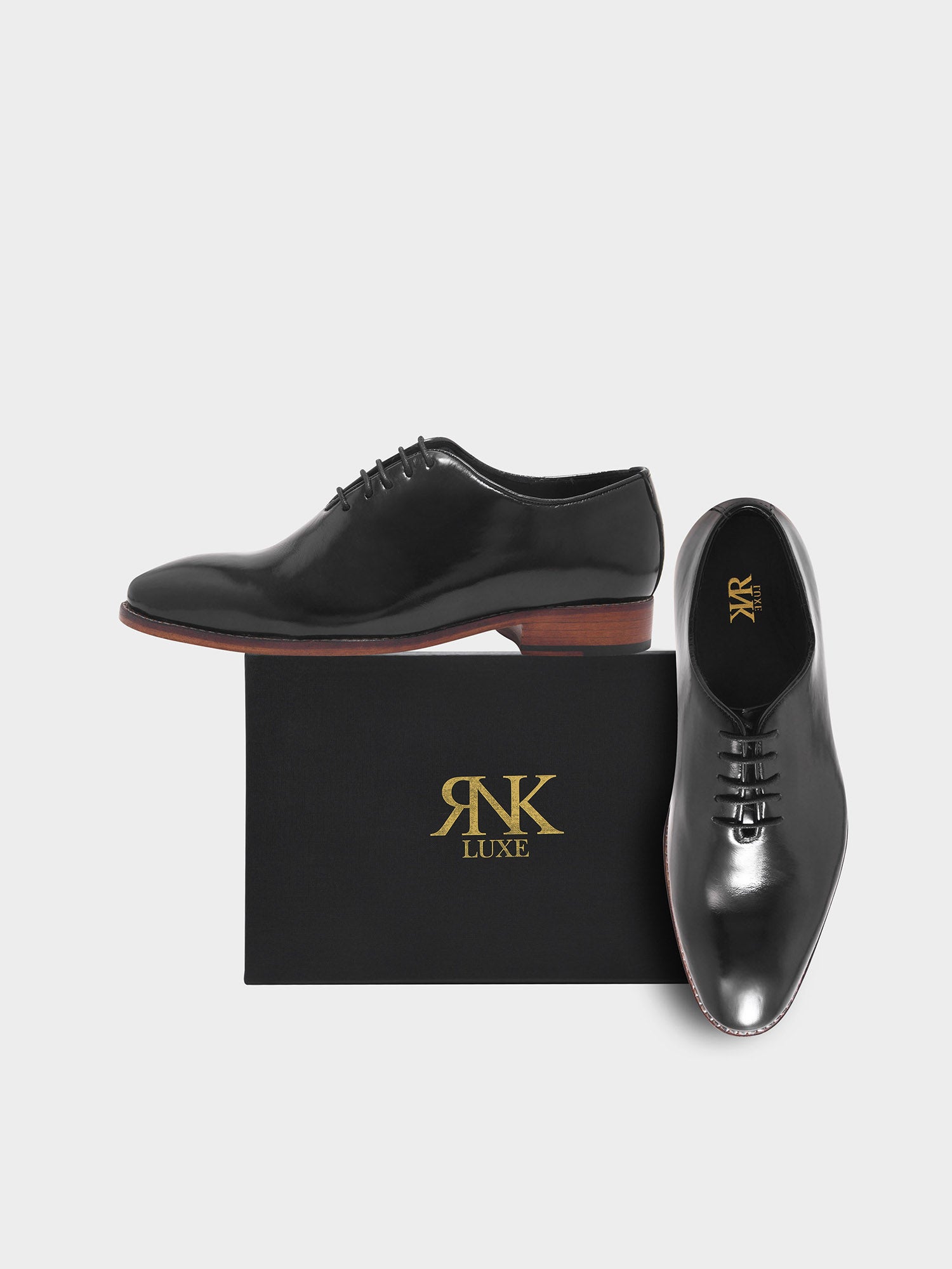 Black dress shoes with brown soles on a black box featuring 'RNK Luxe' branding.