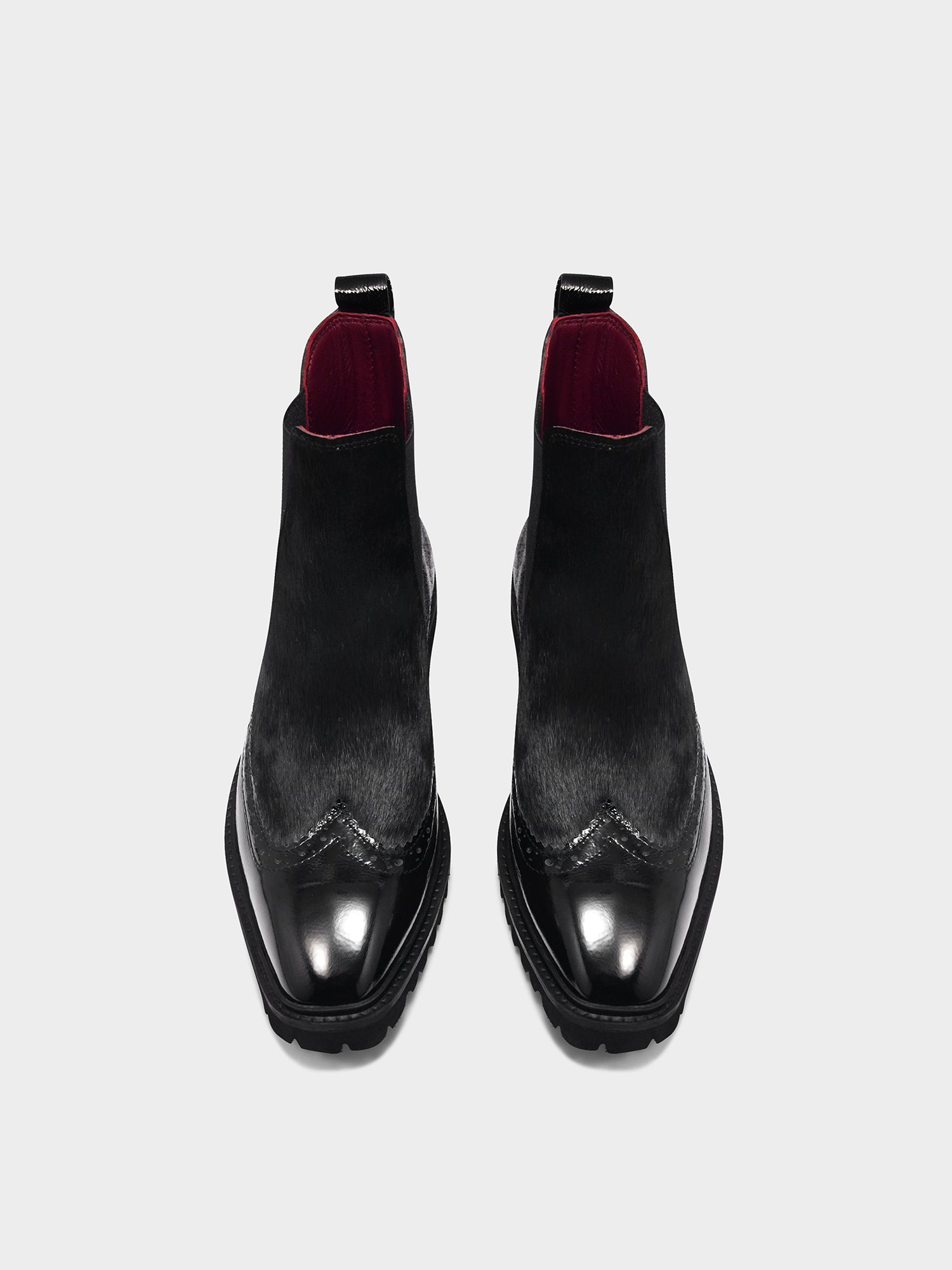 Pair of black leather boots with red soles on a white background