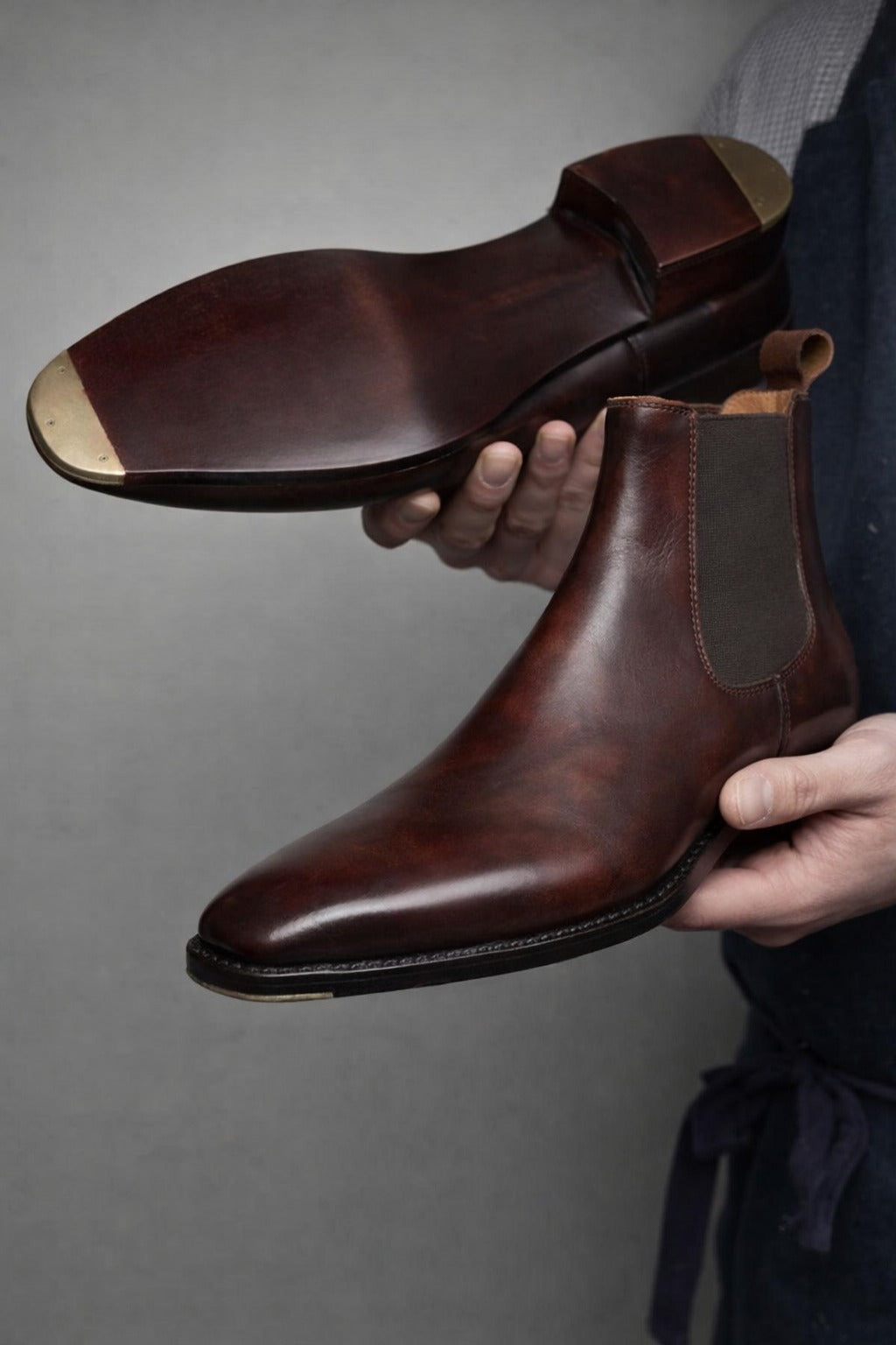 Brown leather shoes held by a person against a gray background