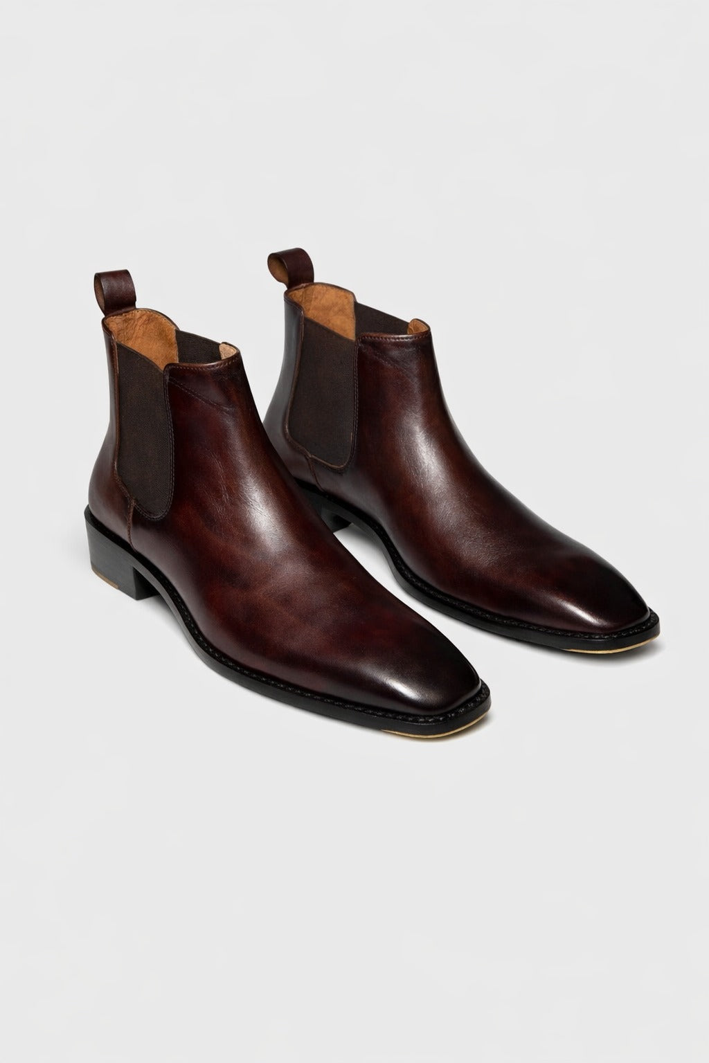 Pair of brown leather Chelsea boots on a light gray background