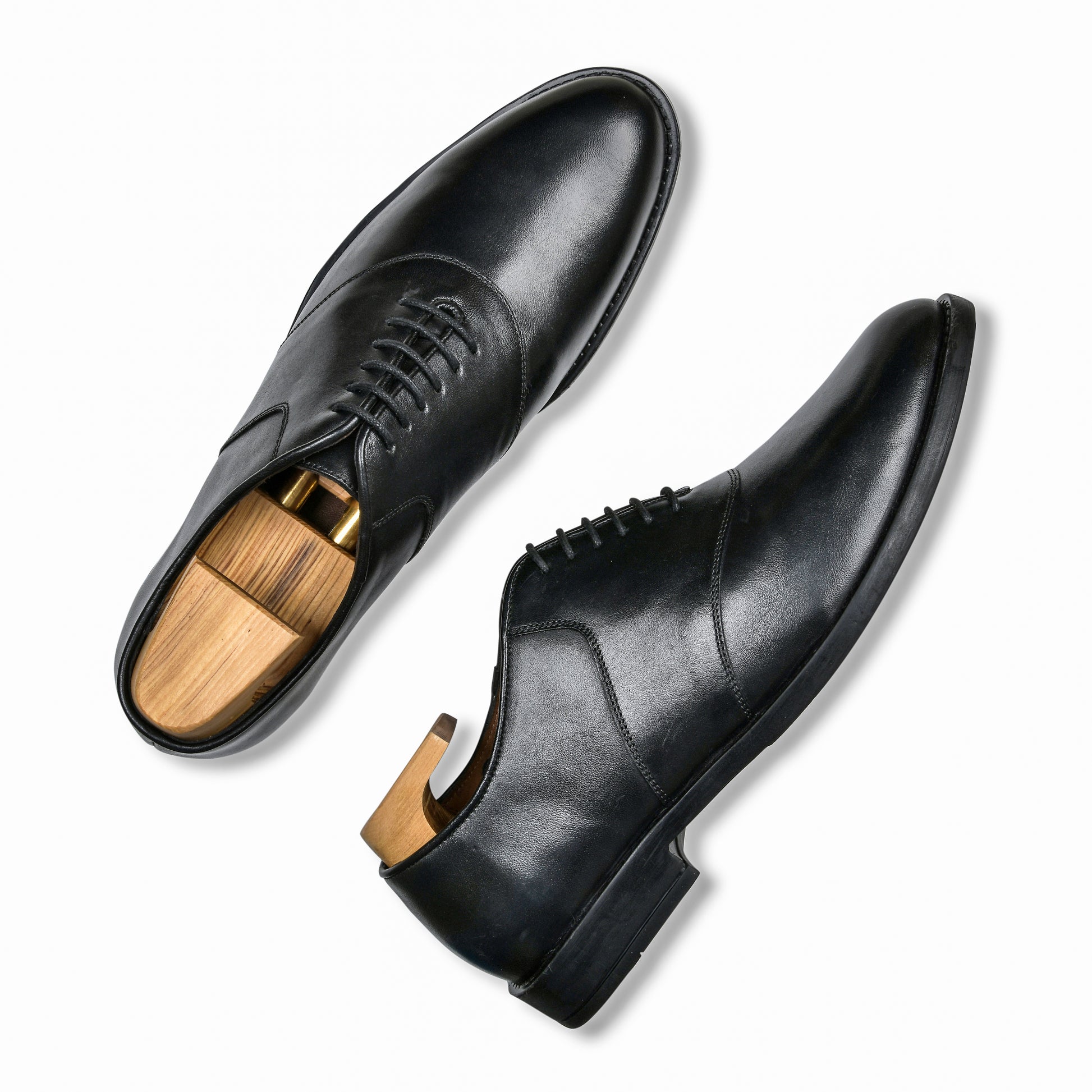 Pair of black dress shoes with wooden soles on a white background