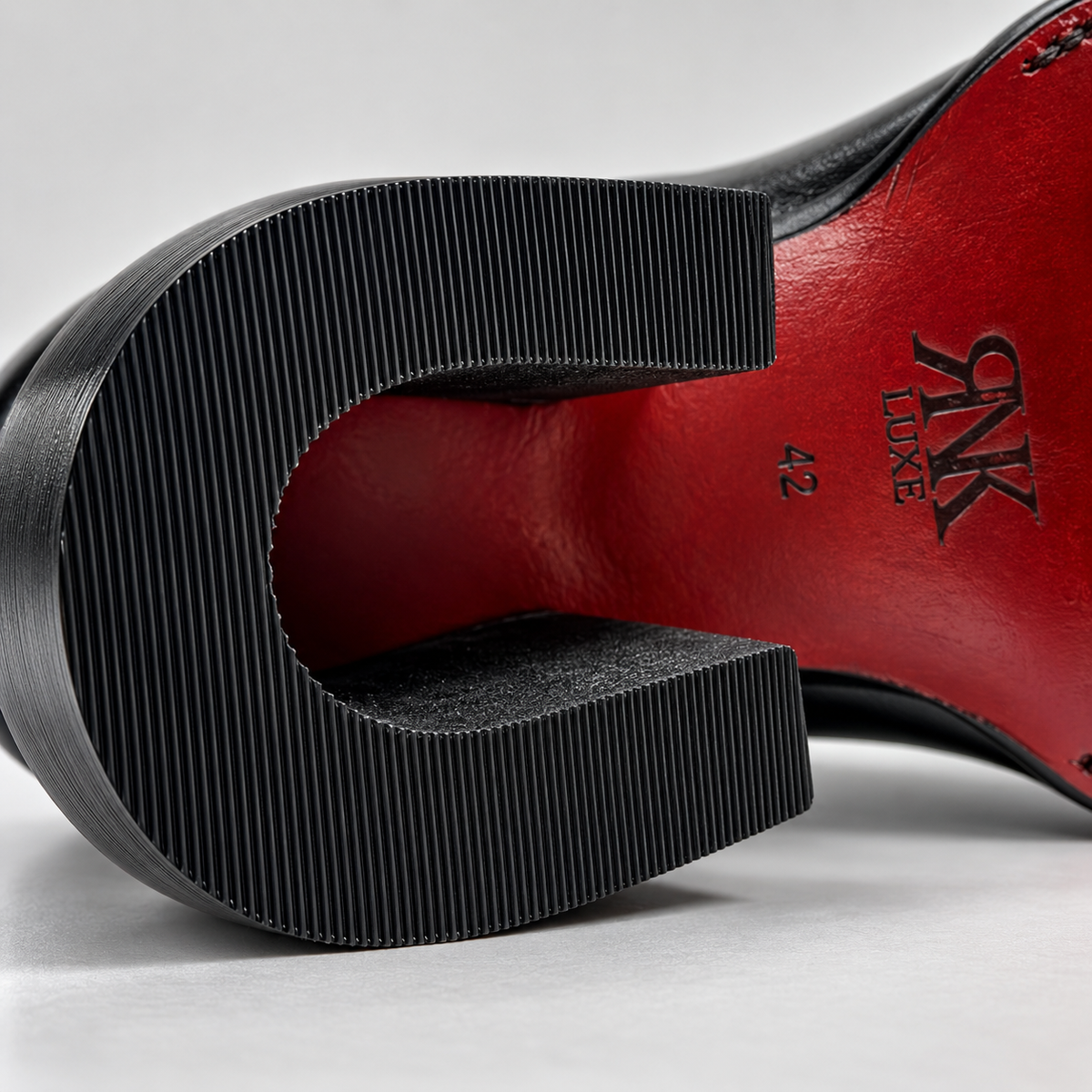 Close-up of the sole of a black leather shoe with a ridged black heel and a bright red insole. The brand name 'PINK LUXE' and size '42' are visible on the red underside.