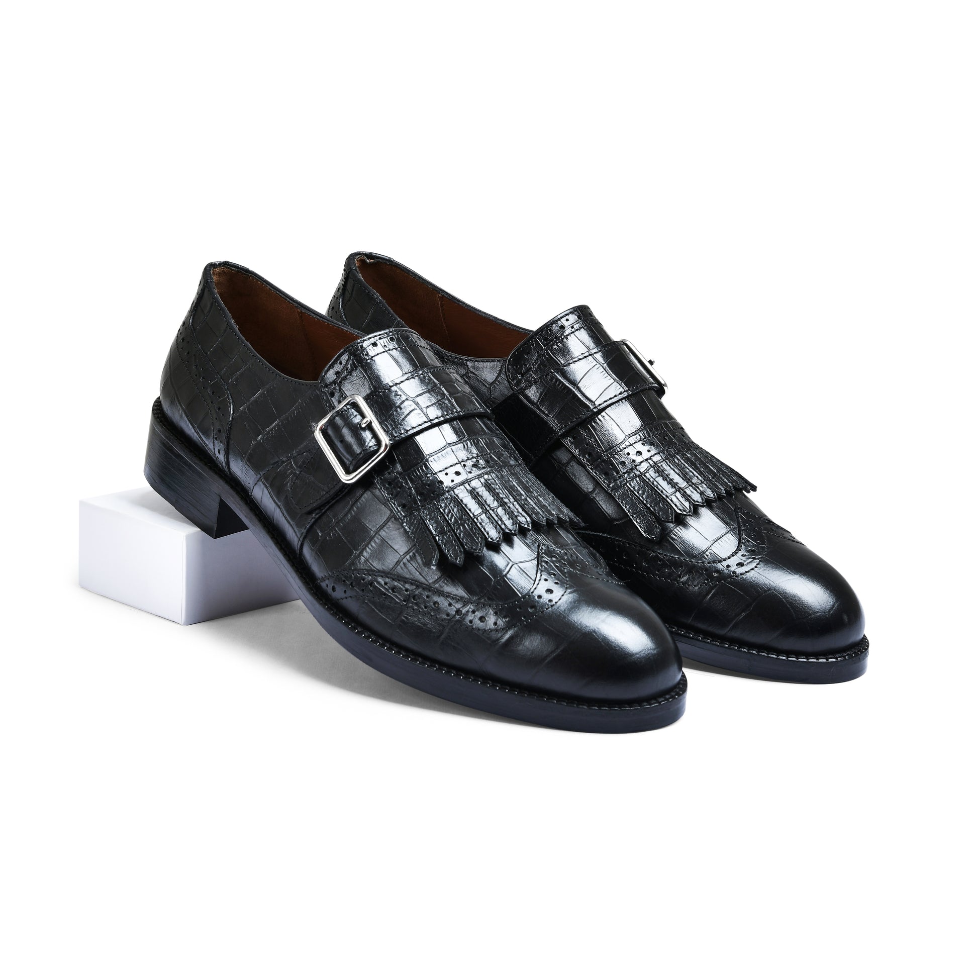 Pair of black leather shoes with fringes and buckles on a white background