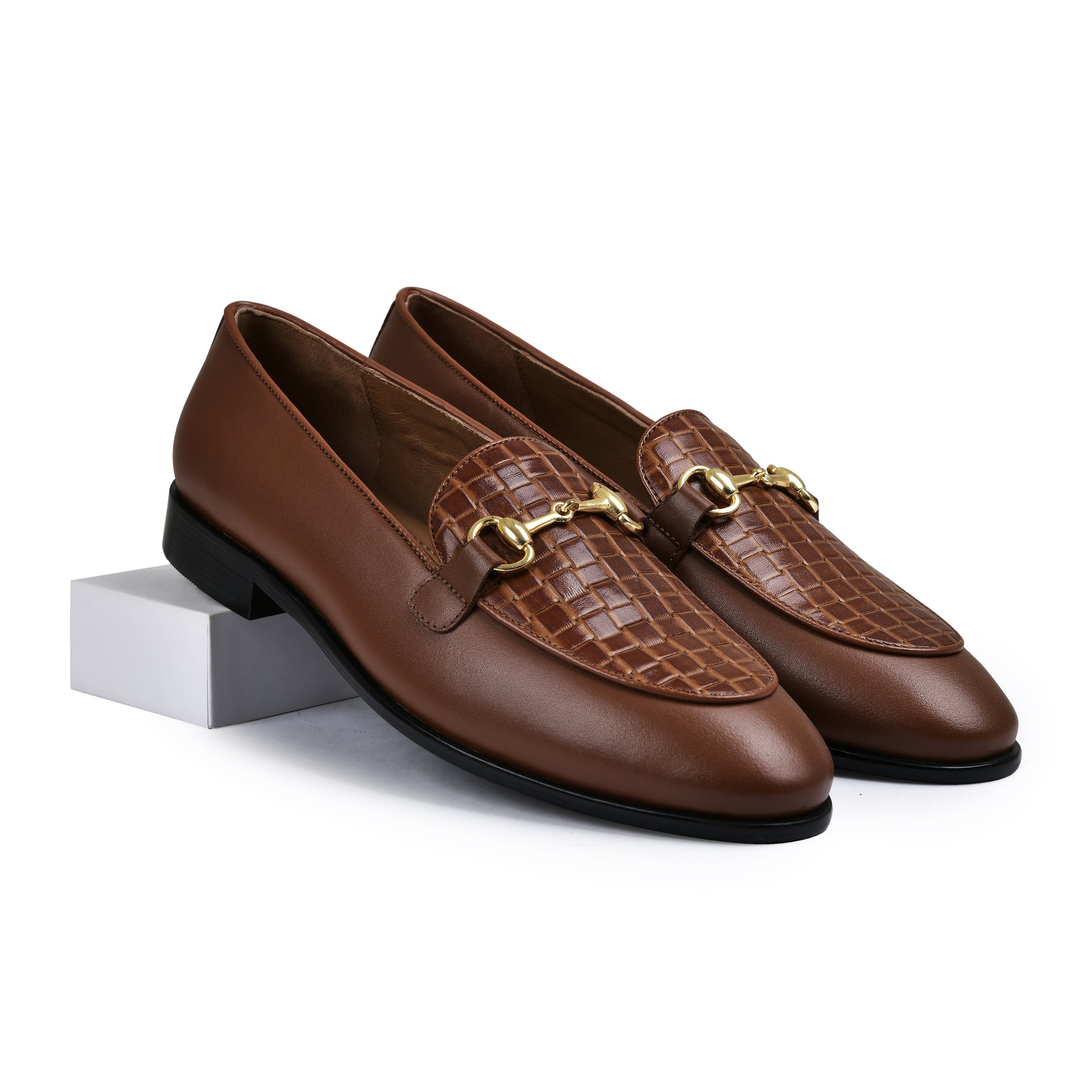 Pair of brown leather loafers with gold accents on a white background