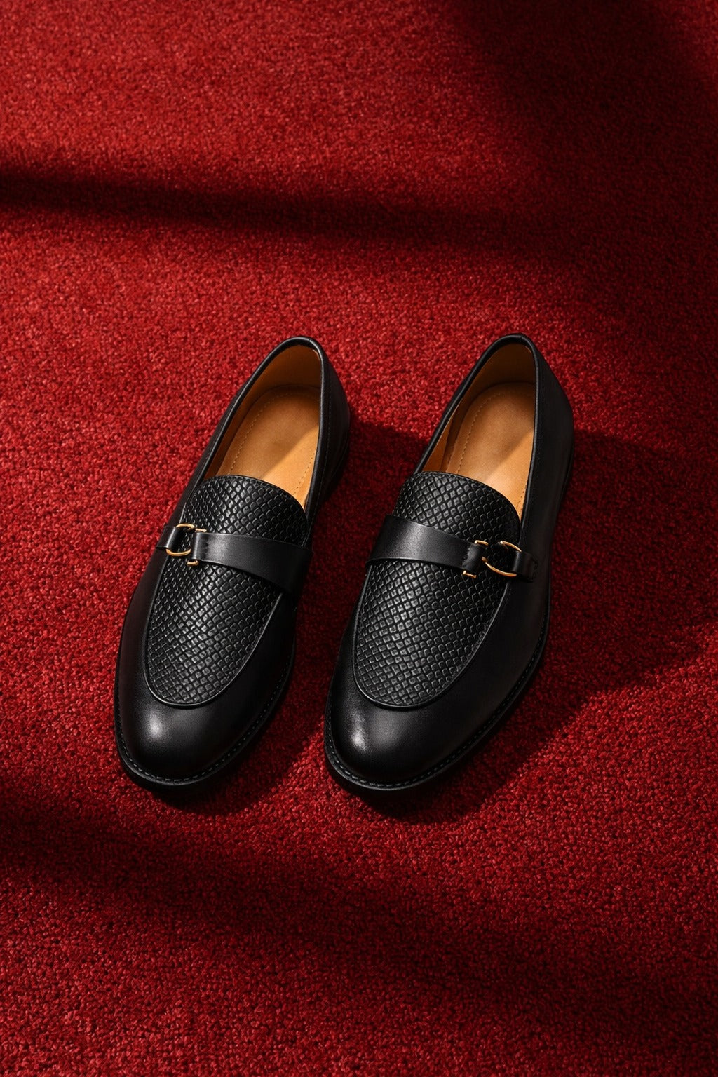 Pair of black leather loafers on a red textured fabric background