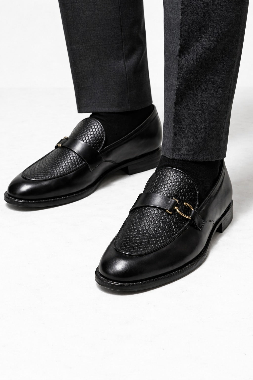 Black leather loafers worn with black pants on a white background