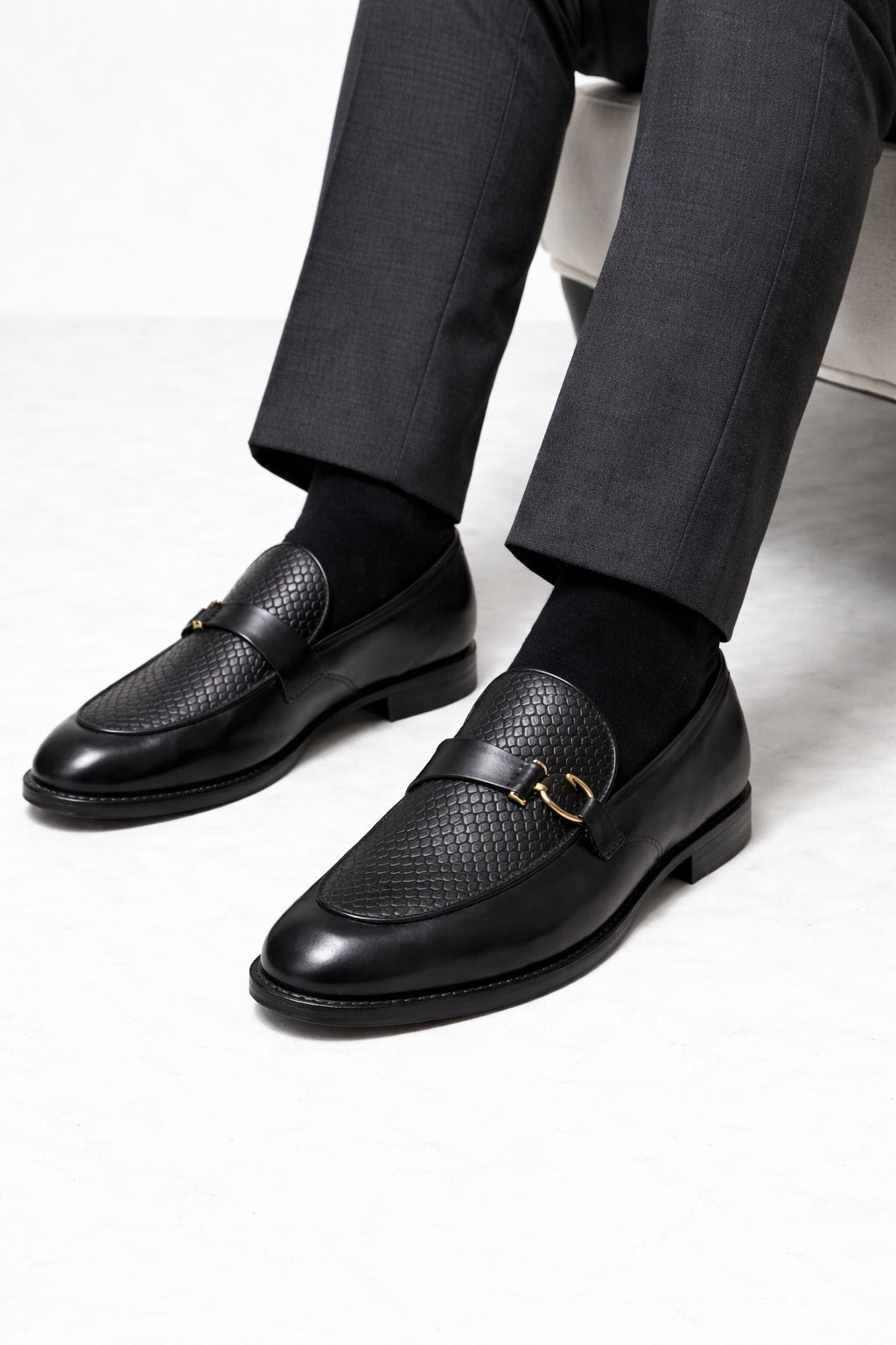 Black leather loafers worn with dark gray pants on a light gray background