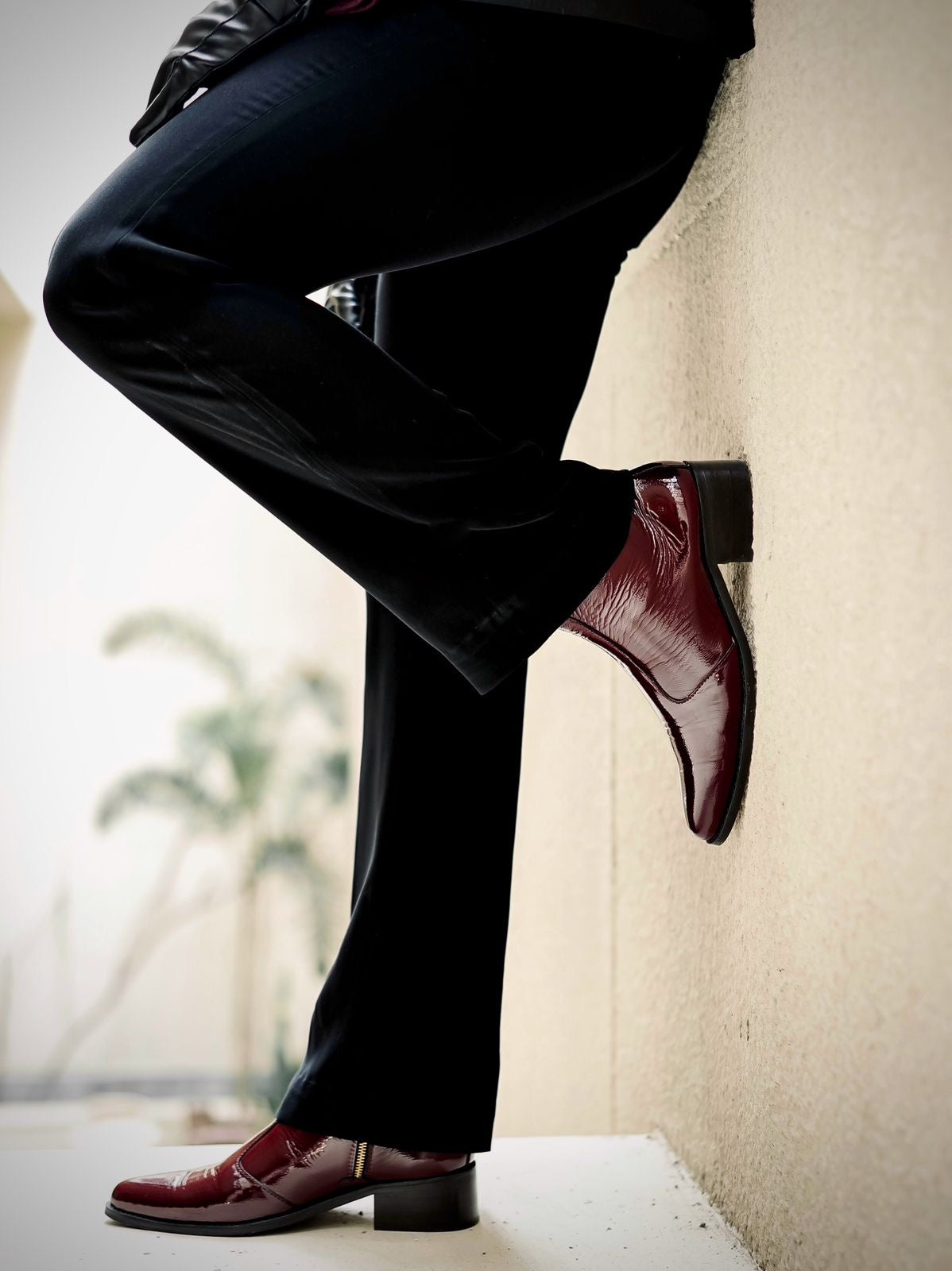 Men’s luxury cherry red pointed-toe Chelsea boots in patent leather with side zip closure, worn with black trousers and leather gloves; sleek and stylish footwear ideal for formal and high-fashion outfits.