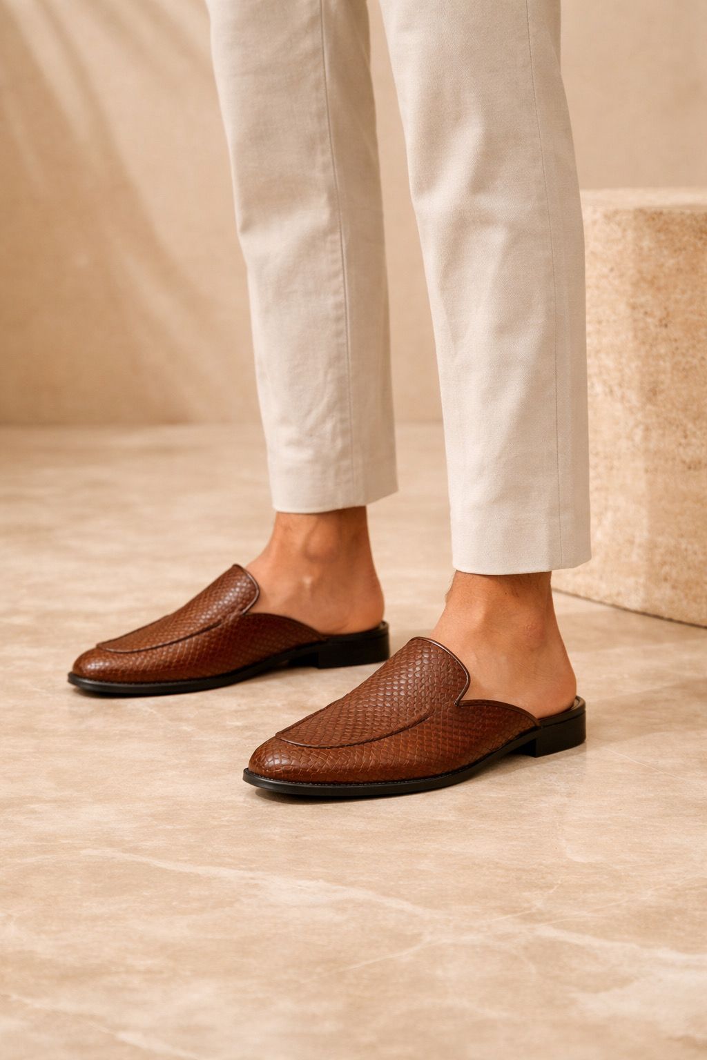Brown woven loafers worn with white pants on a neutral background