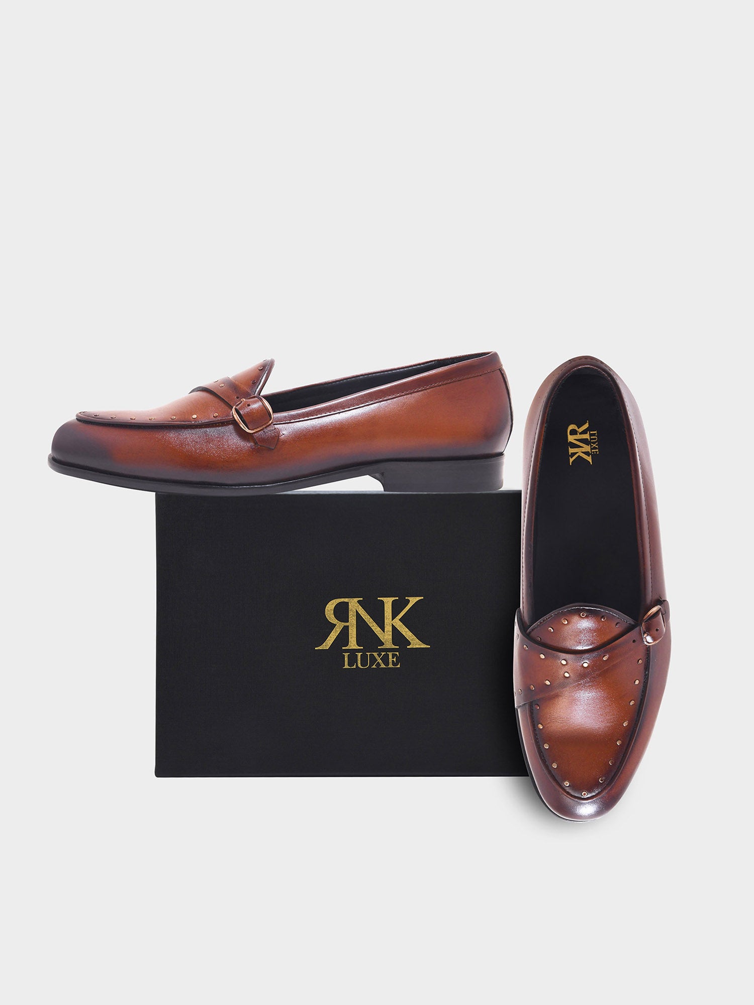 Brown loafers with studded detail on a black box featuring 'RNK Luxe' logo.