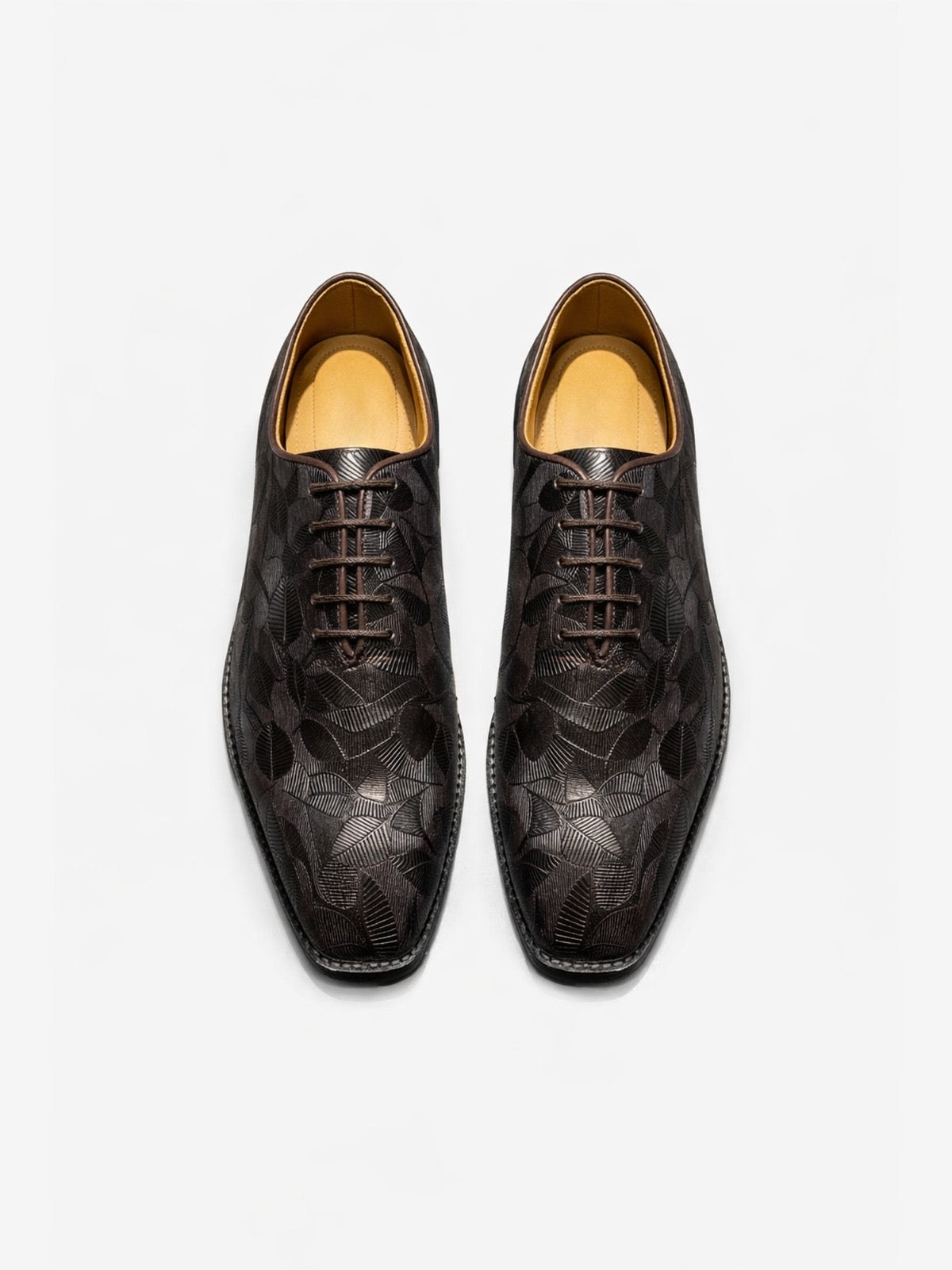 Pair of brown leather shoes with leaf designs on a white background
