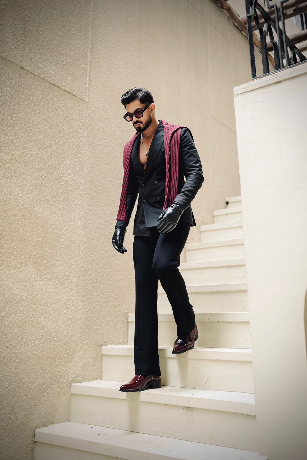 Men’s luxury cherry red pointed-toe Chelsea boots in patent leather with side zip closure, worn with black trousers and leather gloves; sleek and stylish footwear ideal for formal and high-fashion outfits.