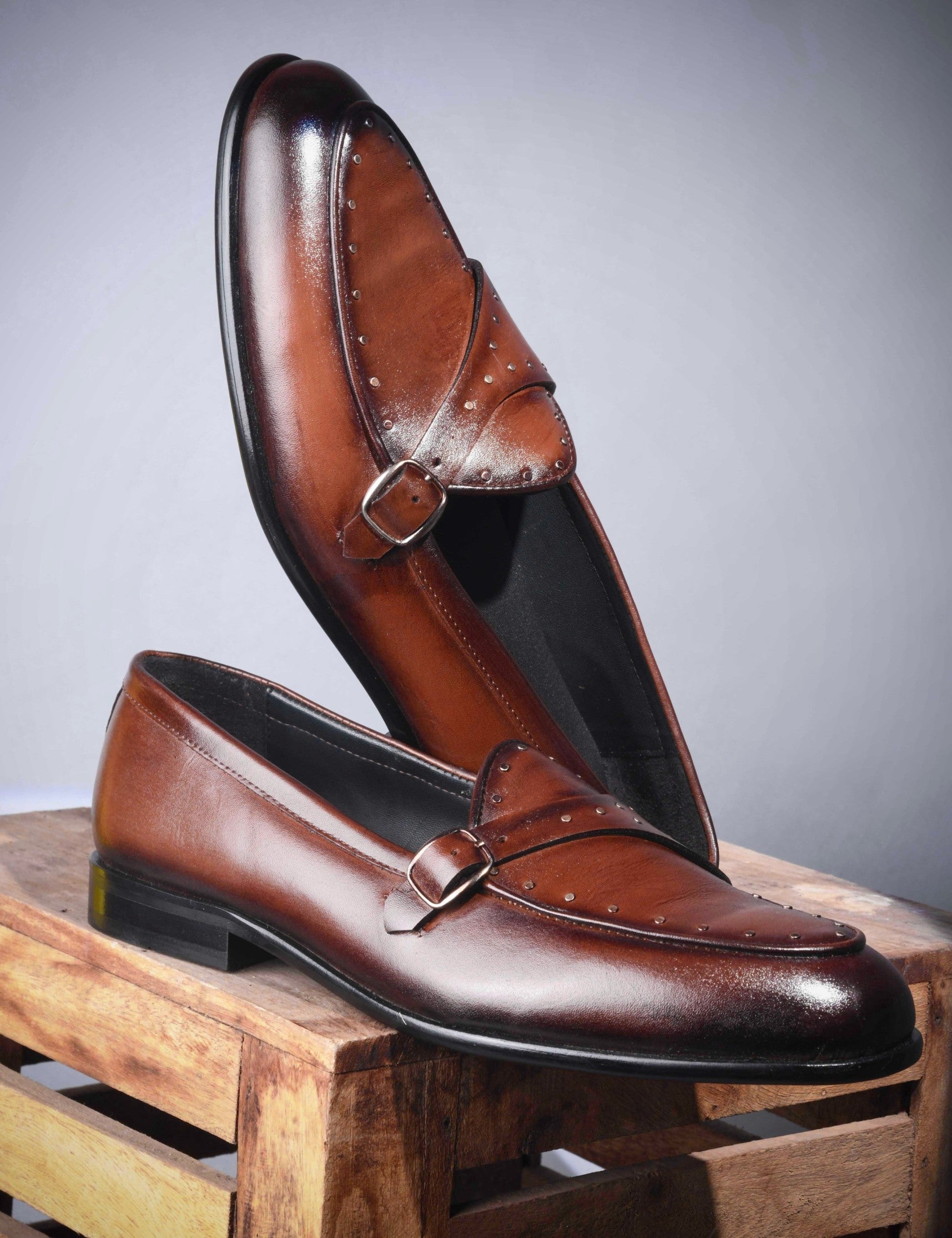 Pair of brown leather loafers on a wooden block with a gray background